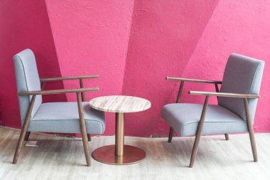 Modern kafe ve restoranın içinde pembe duvar dekorunun yanındaki yumuşak sandalye ve masa..