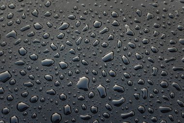 Siyah yüzeydeki su damlacıkları, yansıtıcı ışık duvar kağıdıyla nemli damlaların soyut dokulu arka planı..