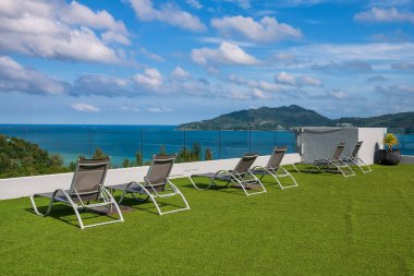 Rooftop bedchairs on fake grass with beautiful view of andaman sea against blue sky, Phuket, Thailand. place to sunbath to get tan at luxury hotel. clipart