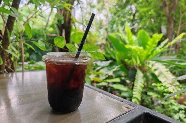 Açık kafeterya bahçesinin üzerinde yeşil ağaç ekili buzlu americano kahvesi..