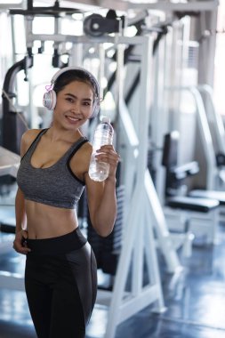 Gülümsemenin gerçek portresi sağlıklı kız spor yaptıktan sonra kırılır. Jimnastik salonunda kulaklık takan güzel, Asyalı, formda genç bir kadın. Vücut geliştirme ve sağlıklı yaşam tarzı konsepti