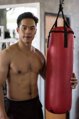 Sporty Asian young man portrait  with punchbag boxing bag in sports gym club. Strong male athlete does exercise, sport clipart