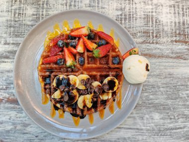 Vanilyalı dondurma, muz, çilek ve böğürtlenli waffle 'lar eski ahşap beyaz masada. Yiyecek ve tatlı endüstrisi.
