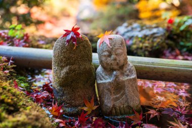 Jizu Buddha statue with colorful maple leaves over head on water basin at Bishamondo autumn garden, Kyoto, Japan. Famous travel destination for tourist in Kansai on peak fall in December. clipart