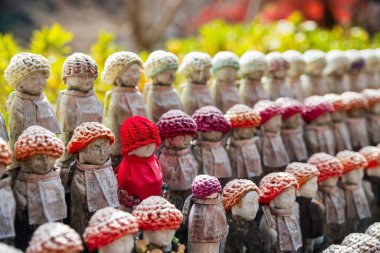 Many Jizu statues in colorful knit hats decor at autumn garden of Hase-dera or Hasedera Temple, Sakurai, Nara, Japan. travel destination for tourist in Kansai on peak fall in December. clipart