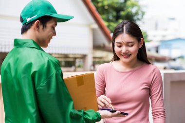 Gülümseyen Asyalı kadın paket kutusunu almak için cep telefonuna imza ya da imza atıyor. İnternet veya cep telefonu uygulaması ile çevrimiçi sipariş için kurye teslimatı.