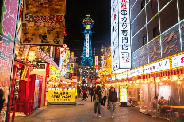  İnsanlar Tsutenkaku Kulesi 'nin Shinsekai Osakas Yeni Dünya restoranını, hediyelik eşya dükkanını ve gece hayatını ziyaret ediyor. Aydınlatılmış reklam panosuyla ünlü bir seyahat yeri.