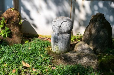 Baharda Japon bahçesinde gülümseyen Jizo Buddha heykeli ve beyaz duvarda açık renk gölgesi. Dış tasarım
