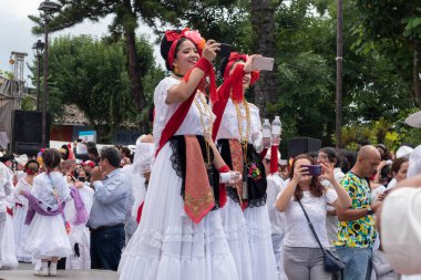 CoATEPEC, VERACRUZ, MEXICO-SEPTEMBER 25, 2022: Veracruz 'dan geleneksel kıyafetlerle giyinmiş iki Latin genç kadın sihirli Coatepec, Veracruz, Meksika' da cep telefonuyla fotoğraf çekiyor