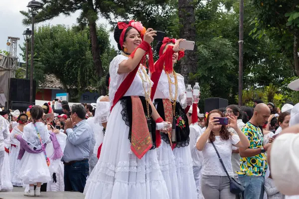 stock image COATEPEC, VERACRUZ, MEXICO- SEPTEMBER 25, 2022: Two latin young women dressed with traditional clothes from Veracruz taking photos with cell phone at magical town of Coatepec, Veracruz, Mexico