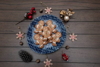 Noel zencefilli adam kurabiyeleri mavi bir tabakta, ahşap bir masada Noel süsleriyle.