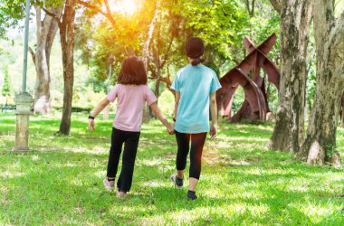 Ilık bahar gününde parkta el ele tutuşan iki kız kardeş. Mutlu arkadaşlık aile kavramı.