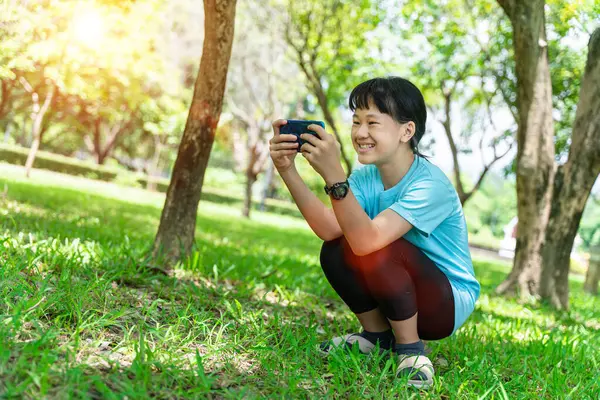 暖かい春の日に公園にいる間に携帯電話を使ってアジア系の少女の肖像画 — ストック写真