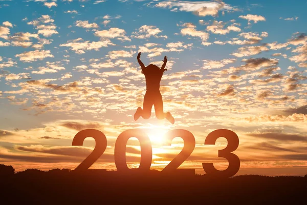 Mutlu yıllar 2023 gün batımında ya da gündoğumunda atlayan kadın silueti.