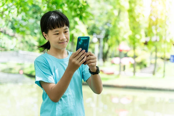 暖かい春の日に公園にいる間に携帯電話を使ってアジア系の少女の肖像画 — ストック写真