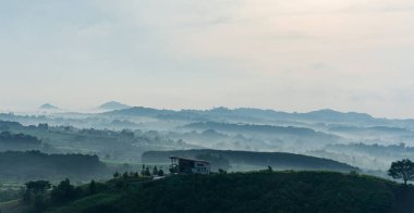 Tepedeki ev. Sisli vadisi ve ufukta uzak dağları olan bir çiftlik evi. Tayland 'ın harika doğa manzarası.