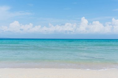 Sandy beach with rolling calm wave of ocean on sunny day on background white clouds in blue sky clipart