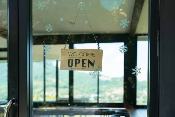 A business sign that says Open on local businesses hang on door at entrance. Say Welcome. Open and closed flip sign in front of shop glass door.