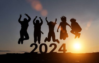 Mutlu bir grup insan 2024 yılının galibiyetini kutluyor. Dost silueti gün batımında dağlarda zıplar.