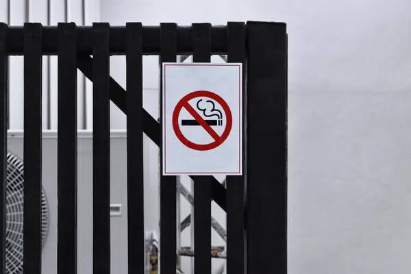No smoking sign. No smoking symbol placard attached to iron fence outside.