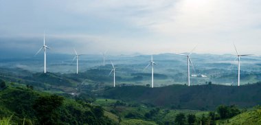 Dağ manzarası ve sisli vadisi ve ufuktaki uzak dağları olan rüzgar türbini çiftliği.