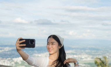 Asyalı kız cep telefonuyla arka planda bulanık bir şekilde selfie çekiyor. Pozitif milenyum içerik oluşturucu video bloğunu etkiledi