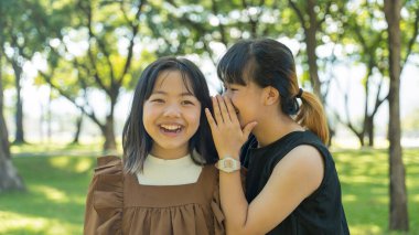 İki kız kardeş kız kardeş parkta kulağına fısıldıyor.