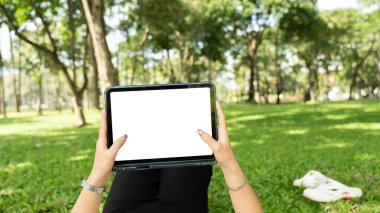 Boş ekran beyaz alan maketi ile tablet pc kullanan kadın el açık havada parkta maket yapıyor.