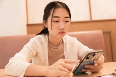 Kafede akıllı telefon kullanan serbest çalışan genç bir kızın portresi.