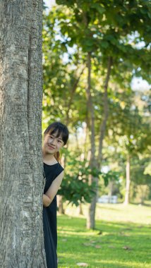 Yeşil parktaki ağacın arkasından bakan kız çocuğu.