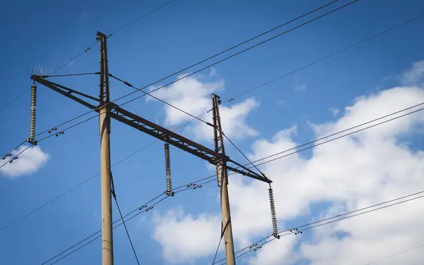 Mavi gökyüzüne karşı yüksek voltajlı kabloları olan kutuplar.