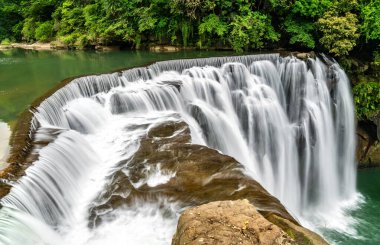 New Taipei, Tayvan 'ın Pingxi ilçesindeki Shifen Şelalesi sık sık Tayvan' ın Küçük Niagara 'sı olarak adlandırılan manzaralı ve sakin bir doğal cazibe sunan yoğun yeşil yapraklar arasında güçlü bir turkuaz havuza dökülür.