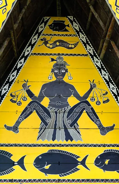 Palau 'da geleneksel bir bai toplantı evinin gablonunda, geometrik motifler ve deniz yaşamlarıyla çevrili sembolik elementler taşıyan stilize edilmiş bir kadın figürü sergileniyor. Cesur siyah ve sarı renk düzeni Palauan 'ı yansıtıyor.