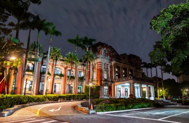 Taipei 'deki Ulusal Tayvan Üniversitesi Hastanesi' nin tarihi kırmızı tuğlalı binası, palmiye ağaçları ve karamsar bulutlu gökyüzü tarafından çerçevelenmiş neoklasik mimariyle gece aydınlandı..