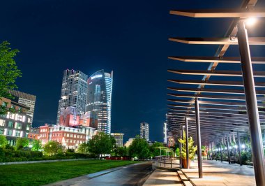 Boston, Massachusetts - 26 Mayıs 2025: Boston 'daki Rose Kennedy Greenway' deki Carolyn Lynch Bahçeleri 'nin gece manzarası, modern binalar ve ışıldayan şehir parkını çerçeveleyen aydınlık yürüyüş yolları.