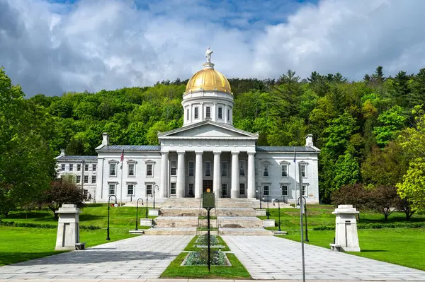 Montpelier 'deki Vermont Devlet Evi' nin ön manzarasında parlak bir bahar gününde yemyeşil ağaçlarla çevrili altın bir kubbe ve neoklasik mimari yer alıyor.
