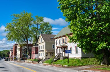 Hallowell, Maine - 25 Mayıs 2025: Renkli 19. yüzyıl binaları Amerika Birleşik Devletleri 'nin küçük nehir kenti Hallowell' de Water Street hattında yer alıyor. Duvar resmi, yapraklı ağaçlar ve klasik tabelalar bu tarihi New England şehir merkezinin cazibesine katkıda bulunuyor..
