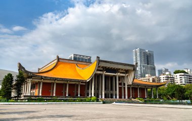 Taipei, Tayvan 'da, Sun Yat-sen Anıt Salonu dramatik gri bulutların altındaki yüksek binalarla çelişen turuncu çatı ve beton sütunlarını gösteriyor..