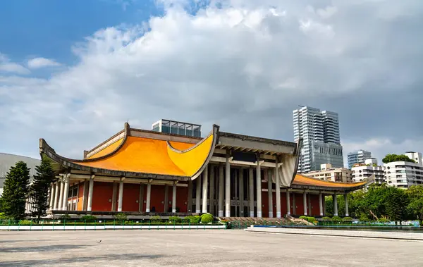 Taipei, Tayvan 'da, Sun Yat-sen Anıt Salonu dramatik gri bulutların altındaki yüksek binalarla çelişen turuncu çatı ve beton sütunlarını gösteriyor..