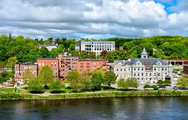 ABD 'nin Maine kentindeki tarihi Augusta şehir merkezine doğru Kennebec Nehri' nin karşısına bakın, Eski Postane, kırmızı tuğlalı binalar ve parçalı bulutlu gökyüzünün altında ağaçlarla kaplı tepeler yer alıyor.