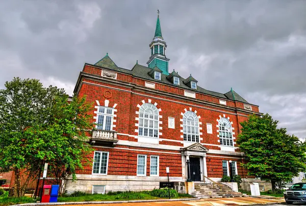 Concord City Hall, New Hampshire, ABD, kırmızı tuğla ön cephe, uzun kemerli pencereler ve dramatik gri bulutlar altında bakır kule ve yemyeşil bahar ağaçları gösterir.
