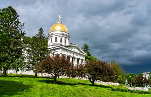 Montpelier 'deki Vermont Devlet Evi' nin ön manzarasında, parlak bir bahar gününde verimli ağaçlarla çevrili altın bir kubbe ve neoklasik mimari yer alıyor.