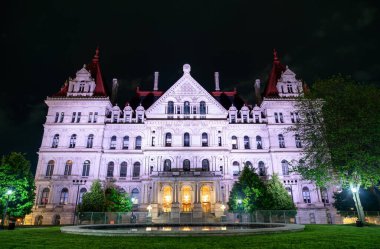 Amerika Birleşik Devletleri 'nin Albany şehrinde süslü New York Eyaleti Kongre Binası karanlık bir gökyüzüne karşı beyaz ve kırmızı parlar dik mansard çatısı ve kemerli pencereleri sessiz bir plaza çeşmesinde aynalıdır..
