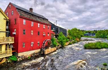 Littleton, New Hampshire, Amerika Birleşik Devletleri 'nde, çalışan bir su çarkı olan kırmızı bir clapboard öğütücü değirmeni Amonoosuc nehrinin üzerinde duruyor parlak, bulutlu bir yaz gökyüzünün altında..