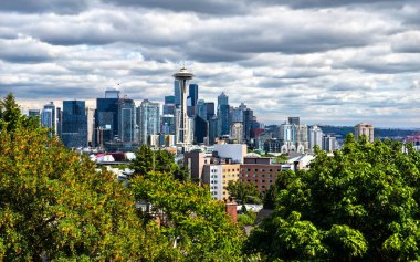 Kerry Park 'tan Seattle gökdelenlerinin ikonik görüntüsü dramatik gökdelenler altında, verimli ön plan ağaçları tarafından çerçevelenmiş