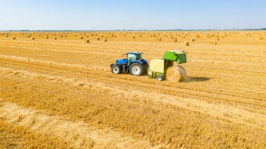 Traktörün yukarısında mercimeği fırına veren makine, kamışı yuvarlıyor ve tarımsal alanın üzerine yuvarlanmış bir balya püskürtüyor..