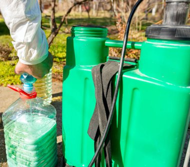 Çiftçi, meyve ağaçlarını mantar veya haşarat hastalıklarından korumak için meyve suyu püskürtmek için plastik sırt çantasındaki böcek ilacının su ve botanik çözeltilerini hazırlıyor..