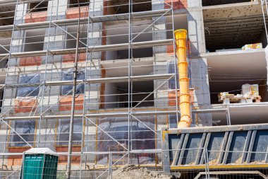İnşaat alanındaki kamyon römorkuna endüstriyel atık atmak için inşaat halindeki binanın yanına yerleştirilmiş sarı uzun plastik boru..       