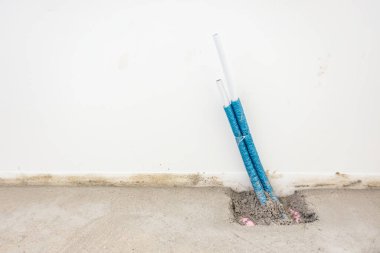 İnşaat halindeki bir binada merkezi ısıtma için döşenmiş beton zeminden izole edilmiş mavi plastik hortumlar çıkıyor..