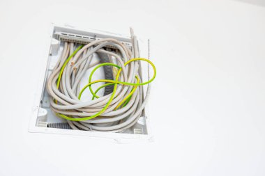 Çeşitli kablolar plastik bir sigorta kutusuna asılmış. Duvara monte edilmiş. Yapım aşamasında olan bir bina. Elektrik kablolarının ve kablolarının kurulumu.